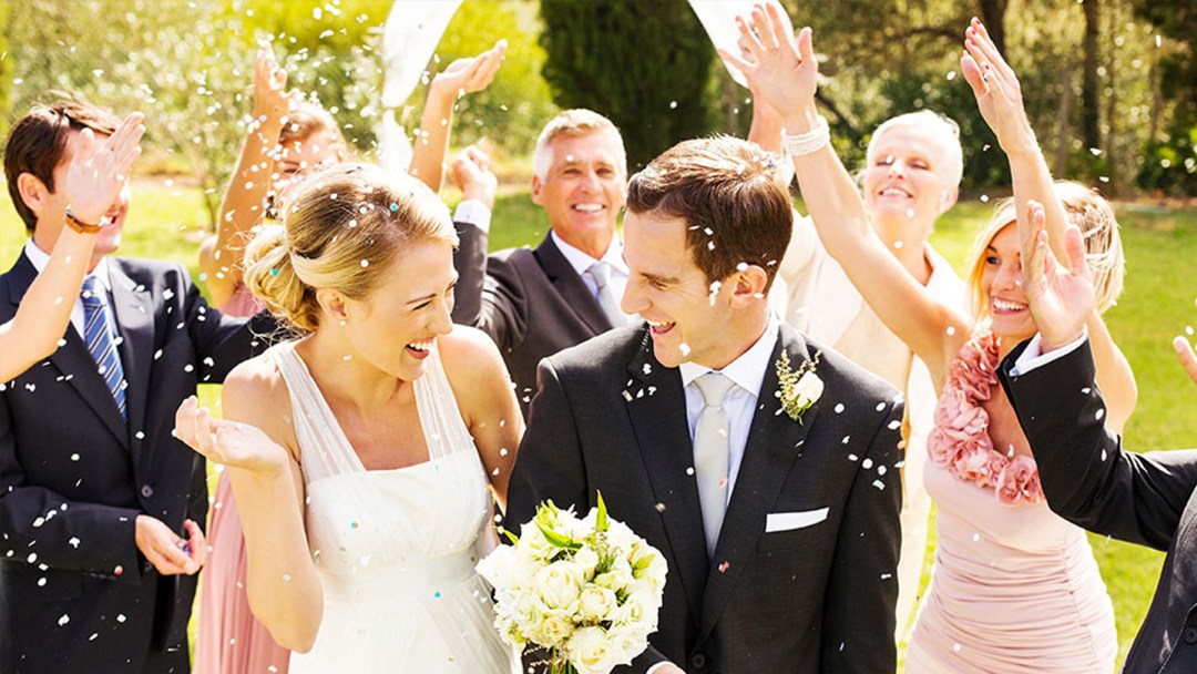 Bride and Groom walking across lawn while wedding party throws confetti
